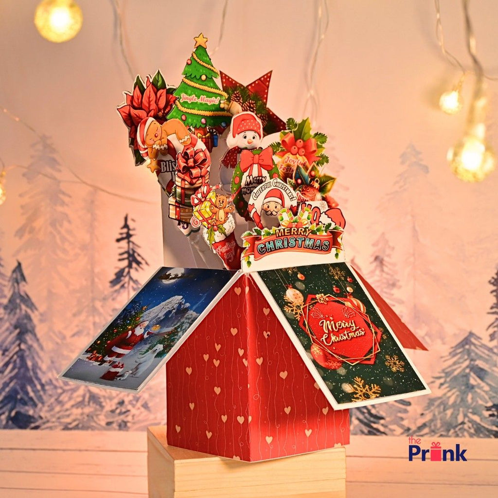 Festive pop-up card box with Christmas motifs like Santa, snowmen, and poinsettias. Background has softly lit fairy lights and snowy trees, creating a warm, joyful atmosphere.